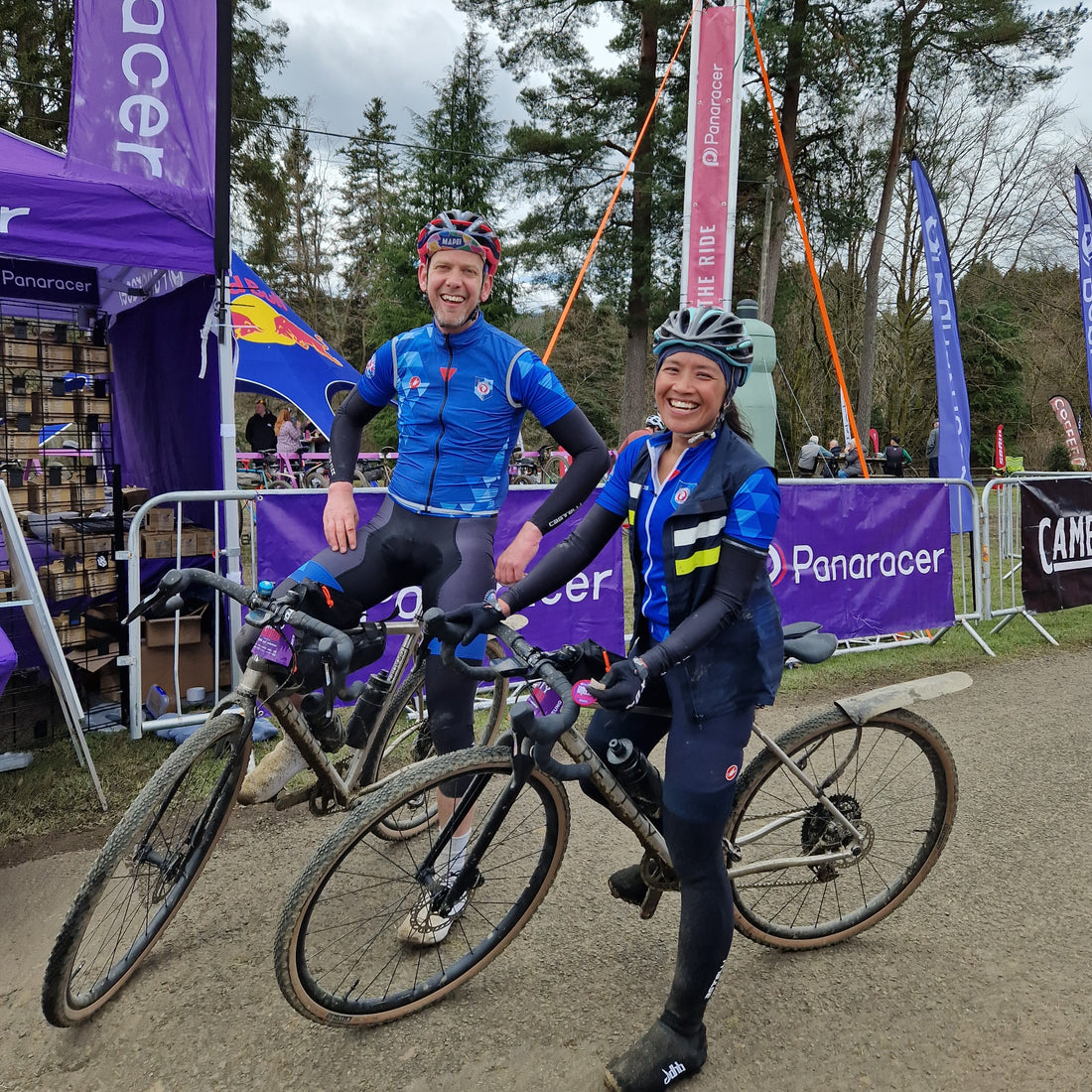 Couple in matching blue jerseys astride bikes smile at the camera.