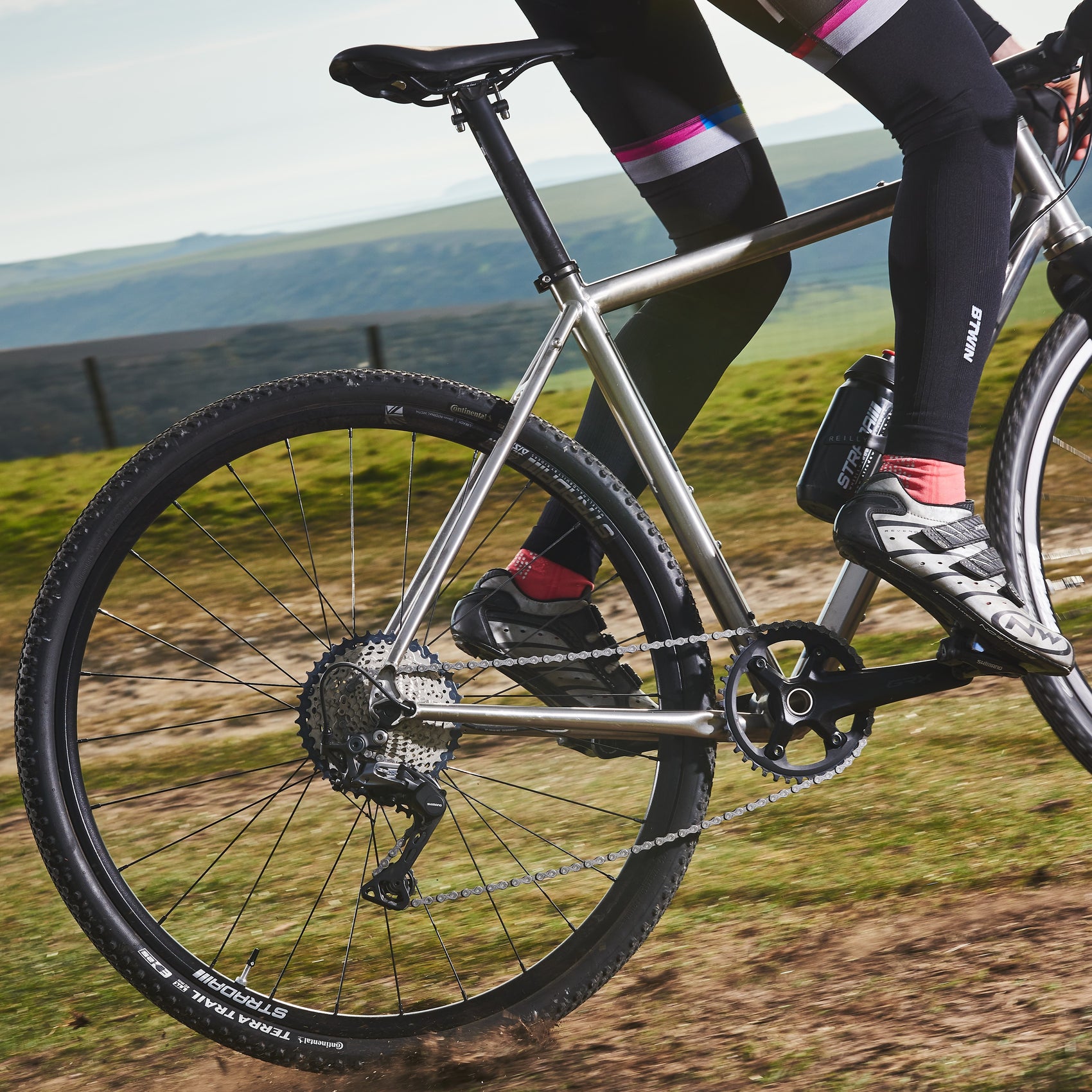 Back wheel of titanium bike as cyclist rides uphill