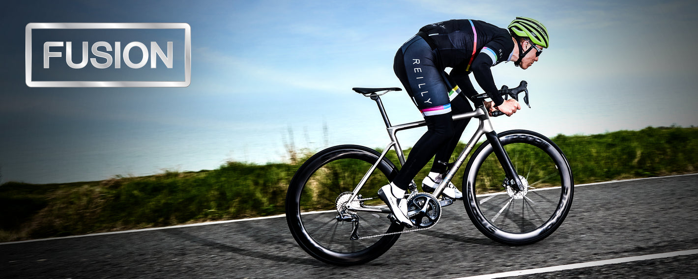 Side view of male cyclist going uphill on a titanium road bike. FUSION is written top left.