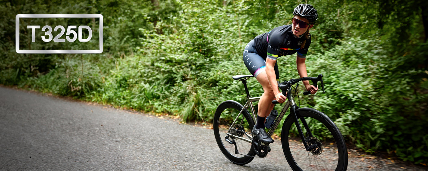 Girl on bike looks to left as she cycles along a paved road with bushes.  T325D is top left.