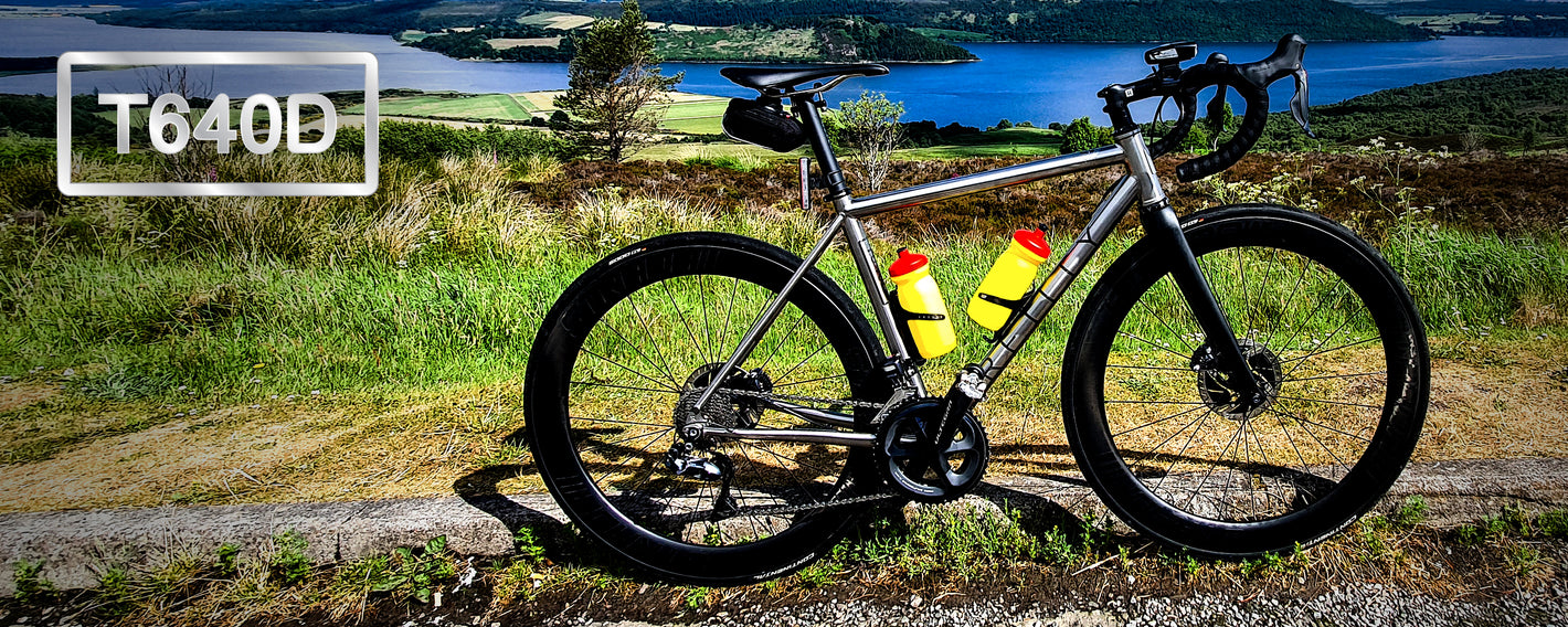 Road Bike in the foreground with beautiful green landscape and lake in the background. T640D is written top left. 