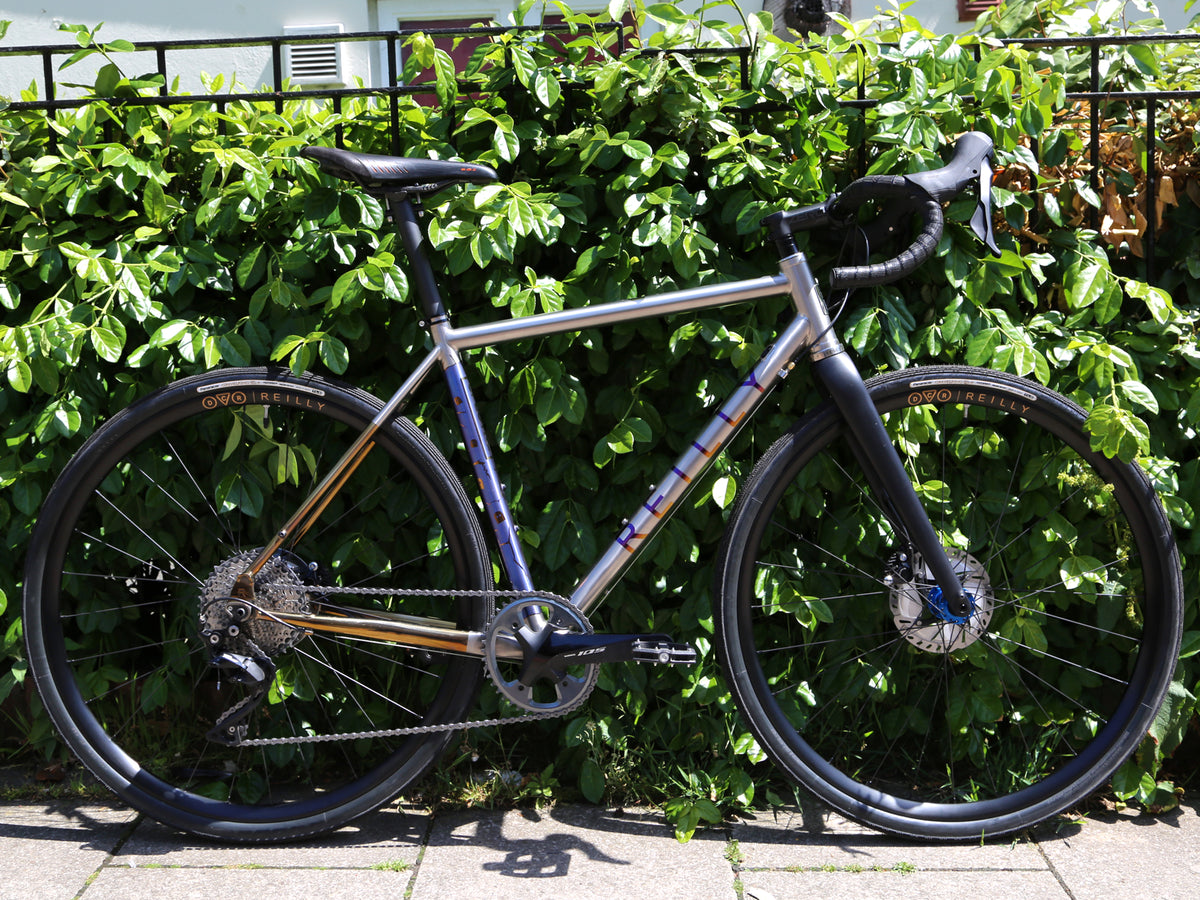 Reilly Spectre with purple logo and blue anodised seat tube, gold anodised seat stays, blue hubs and DCR wheels.  Against a green bush. 